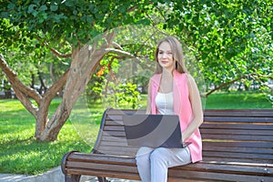 Beautiful woman sitting on a park bench using a laptop.