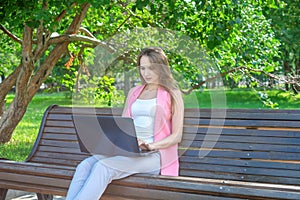 Beautiful woman sitting on a park bench using a laptop.