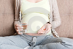 Beautiful woman sitting on sofa holding a pill and water
