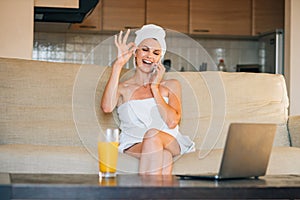 Beautiful woman sitting on the sofa at home using smartphone doing happy thumbs up gesture with hand. approving