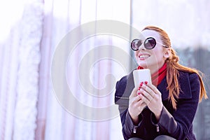 Beautiful woman sitting at the street holding her mobile phone smiling