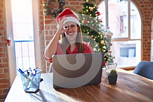 Beautiful woman sitting at the table working with laptop wearing santa claus hat at christmas doing ok gesture with hand smiling,