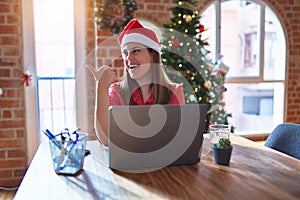 Beautiful woman sitting at the table working with laptop wearing santa claus hat at christmas smiling with happy face looking and