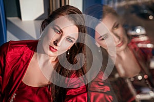 Beautiful woman sitting at the window in a red negligee, brooding view