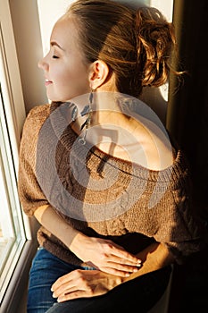 Beautiful woman sitting on the window sill and looking somewhere