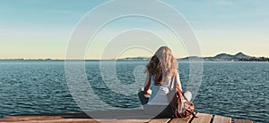 Beautiful woman sitting on wooden pier and looking at the sea