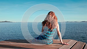 Beautiful woman sitting on wooden pier and looking at the sea