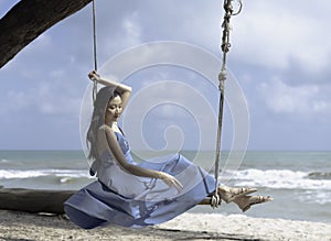 Beautiful woman sitting on wooden Swing on the beach