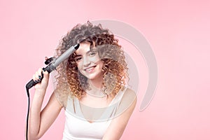 Beautiful woman with a smile on her face with amazing curls in a white T-shirt is doing styling in her hand holding