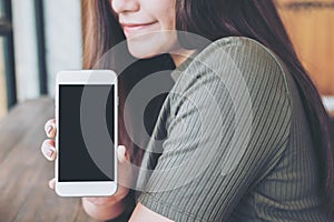 A beautiful woman with smiley face holding and showing white mobile phone with blank black screen in vintage wooden cafe