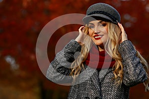 Beautiful woman smiling in autumn park and looking at camera. Red maple garden background