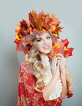 Beautiful woman smiling and holding fall leaves in hands. Pretty model with makeup, curly hair, autumn leaves crown