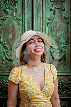 Beautiful woman smiling in a yellow dress and white hat in front of an antique colonial style green door