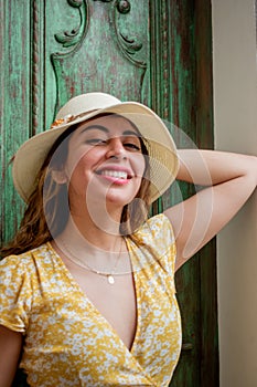 Beautiful woman smiling in a yellow dress and white hat in front of an antique colonial style green door
