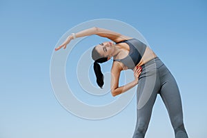 Beautiful woman in sportswear doing her stretches. Over blue sky. Upward angle