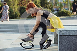 Beautiful woman in sportswear jumping in a kangoo jumps shoes at the street on summer`s sunny day