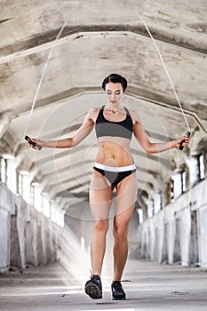 Beautiful woman in sportswear doing exercise with skipping rope in the abandoned industrial building