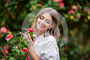 Beautiful woman with spring blooming pink flowers. A young smiling girl enjoys the pink flowers of a rose. Summertime.