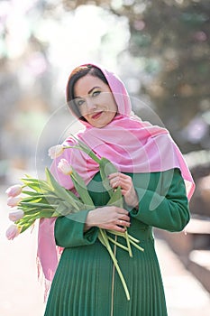 Beautiful woman with spring tulips flowers bouquet at city street. Happy portrait of girl smiling with pink tulip