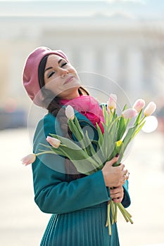 Beautiful woman with spring tulips flowers bouquet at city street. Happy portrait of girl smiling with pink tulip