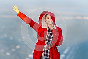 Beautiful woman stand near cliff with hold coat hood and wave hand on the mountain with warm light of sun rise and she look