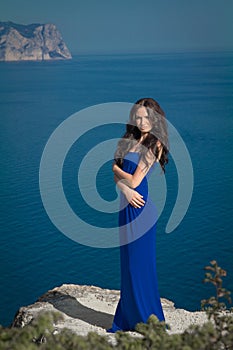 Beautiful woman standing on a cliff over blue sky. Brunette girl