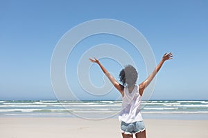 Beautiful woman standing with open arm at beach on sunny day