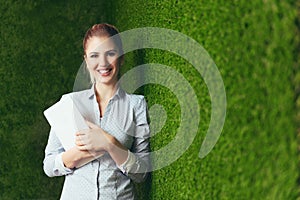 Beautiful woman standing over a green grass wall, holding a tablet