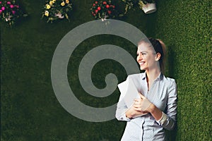 Beautiful woman standing over a green grass wall, holding a tablet