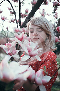 Beautiful woman standing among sakura branches, pretty girl relaxing outdoor. Soft pink colours. Close-up.