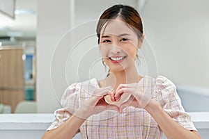 beautiful woman standing smiling doing heart shaped hands in room