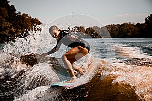 Beautiful woman stands with bent knees on surf style wakeboard and ride on wave