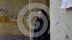 A beautiful woman stands in the ghetto, against a dumbfounded wall. A girl in street clothes stands alone and looks into