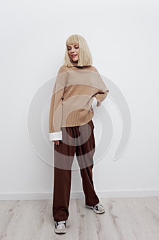 a beautiful woman stands half sideways in full height on a light background in a sweater and shirt, putting her hand on