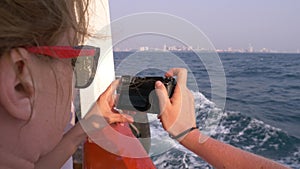 A beautiful woman stands at the stern of the ship and makes a video on the camera. Waves in the background