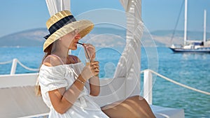 Beautiful woman in straw hat sitting on the wooden sea pier, drinking orange juice or cocktail and enjoying view of the