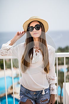 Beautiful woman in straw hat and sunglasses luxury relaxing on hotel terrace enjoying sun on blue sky sea outdoors background