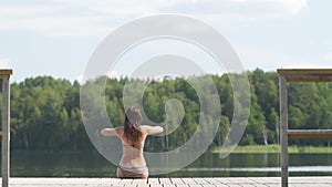 A beautiful woman stretches on the pier. The girl stretches before swimming on the lake.