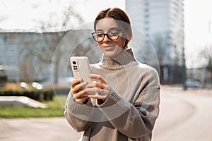 Beautiful woman student in eyeglasses using a phone in the street. Safe and happy