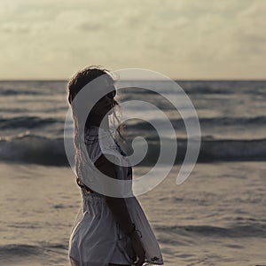 Beautiful woman in summer dress standing in ocean on sunset evei