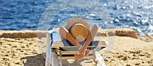 Beautiful woman sunbathing on a beach at tropical travel resort, enjoying summer holidays. Girl lying on sun lounger near the sea