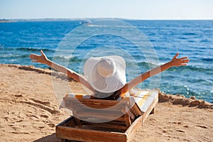 Beautiful woman sunbathing on a beach at tropical travel resort, enjoying summer holidays raising her hands up. Young