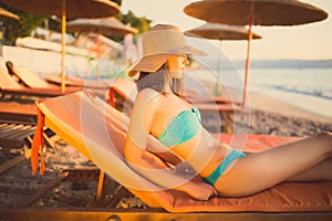 Beautiful woman sunbathing in a bikini on a beach at tropical travel resort,enjoying summer holidays.Young woman lying on sun bed