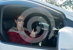 Beautiful woman with sunglasses sit in car and look at camera through window with show thumbs up in concept of safe drive on the