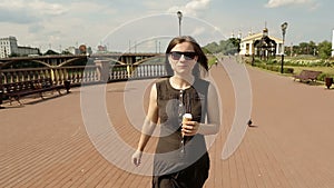 Beautiful woman in sunglasses on street walking and eating ice cream. Steadycam
