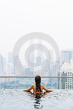 Beautiful woman in swimming pool watching the city