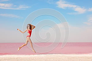 Beautiful woman in swimsuit jumping near pink lake