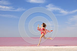 Beautiful woman in swimsuit jumping near pink lake