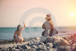 Beautiful woman in a swimsuit walking along the beach against the background of a pyramid of stones. Blurred female with stones on