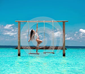 Beautiful woman swinging in the Indian Ocean over tropical landscape, Maldives island background